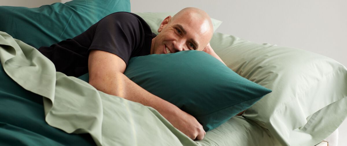 Man laying in green linen bedding
