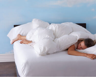 Woman laying in bed under fluffy white comforter