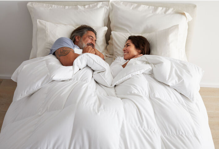 Man and woman snuggling under white comforter