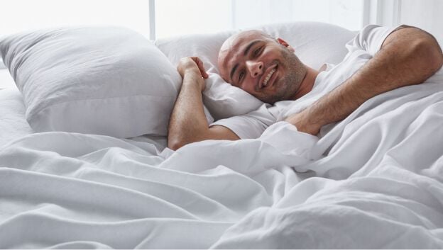 Image of a man laying in white linen bedding